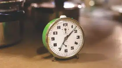 Assiette vide et verre d'eau à côté d'une horloge affichant 16h sur une table de cuisine