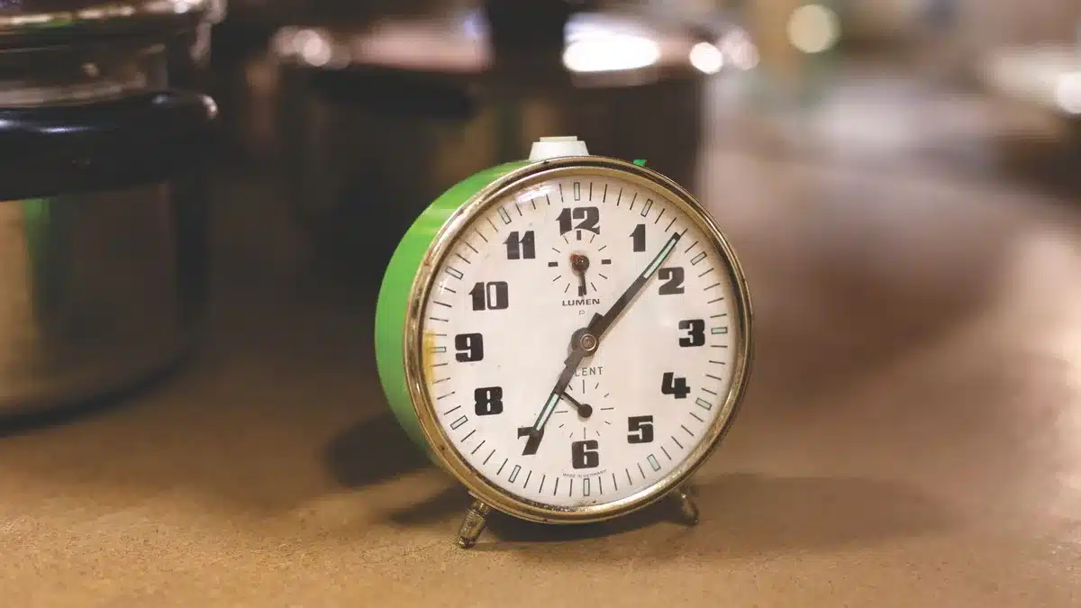 Assiette vide et verre d'eau à côté d'une horloge affichant 16h sur une table de cuisine