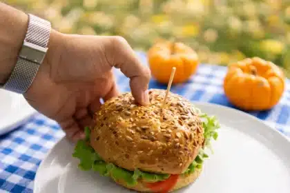 Mains tenant des graines de courge au-dessus d'un bol, avec des fruits frais et une tasse de thé sur une table