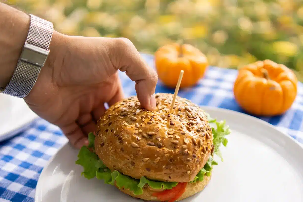Mains tenant des graines de courge au-dessus d'un bol, avec des fruits frais et une tasse de thé sur une table