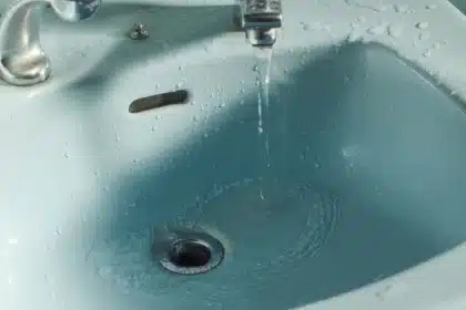Mains tenant une cup menstruelle transparente au-dessus d'un lavabo de salle de bain avec de l'eau