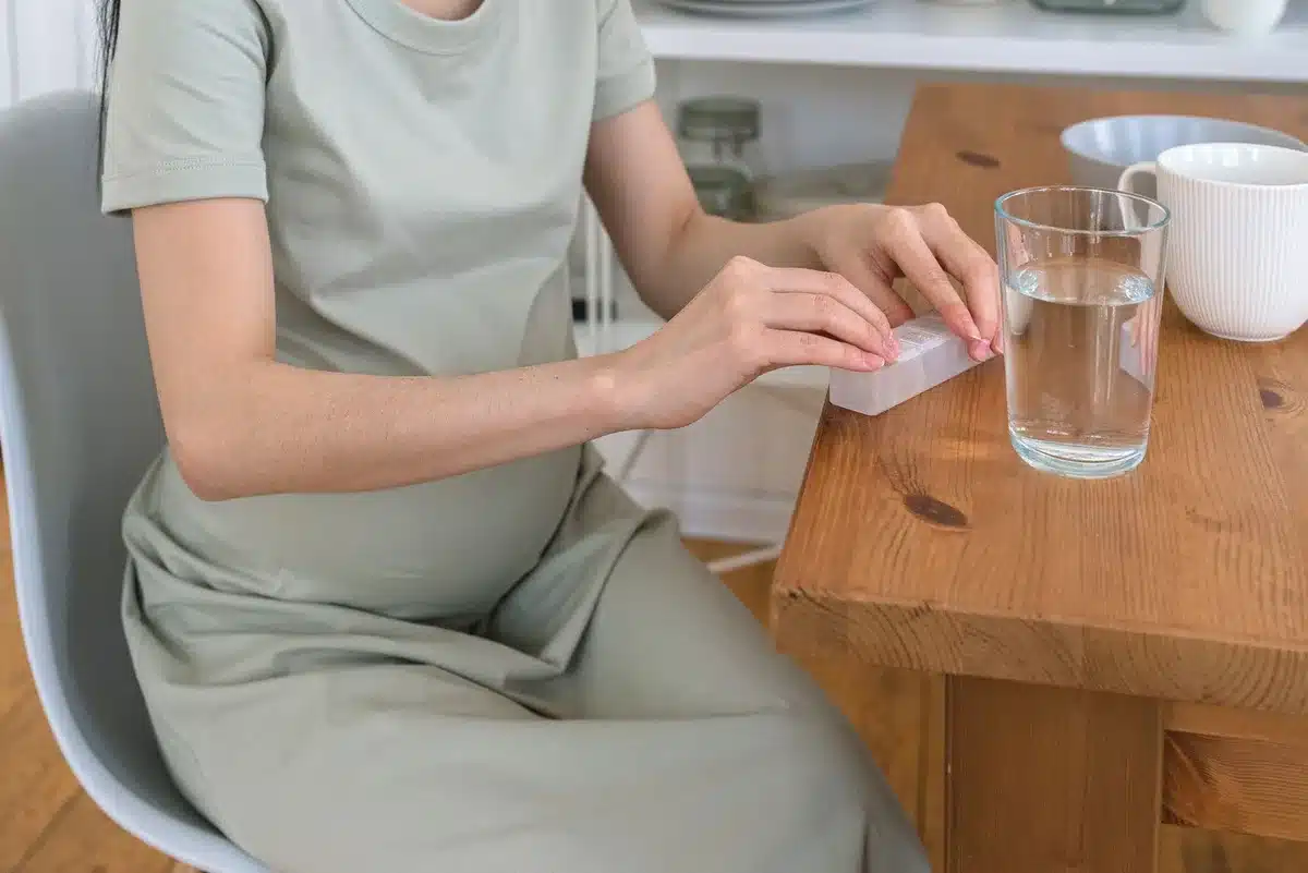 Une femme enceinte tenant un flacon de vitamines pr&eacute;natales