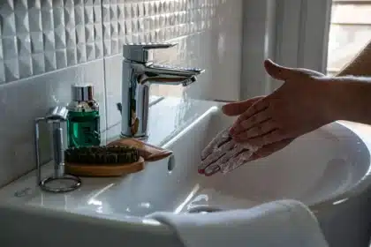 Mains se lavant sous l'eau tiède courante dans une salle de bain, illustrant une hygiène douce et régulière.