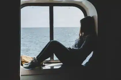 Silhouette d'une personne assise seule face à une fenêtre, contemplant l'extérieur dans un environnement calme