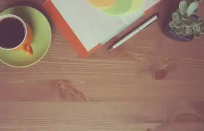 Mains anonymes posées sur une table de cuisine ensoleillée avec un carnet et une tasse