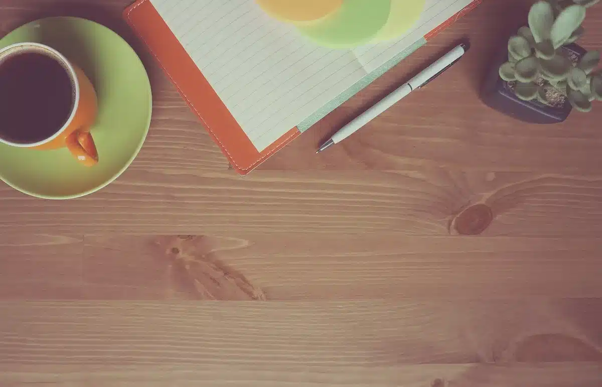 Mains anonymes posées sur une table de cuisine ensoleillée avec un carnet et une tasse